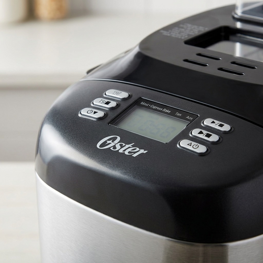 A detailed macro photograph focusing on the textured control buttons, the digital display, and the "Oster" logo of the bread maker.