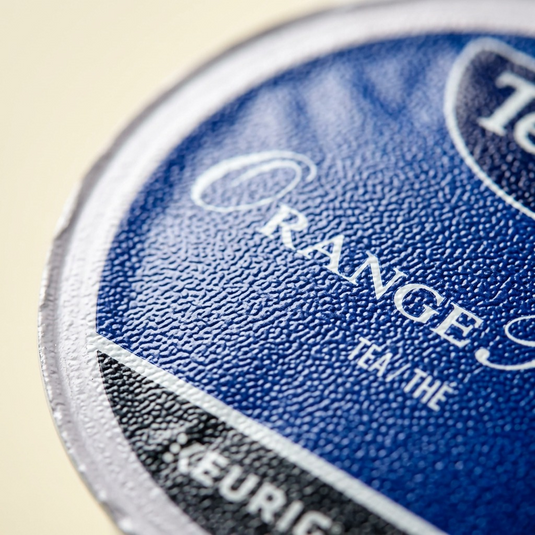 Macro close-up capturing the fine foil texture and precise logo printing of a Tetley Orange Pekoe K-Cup.