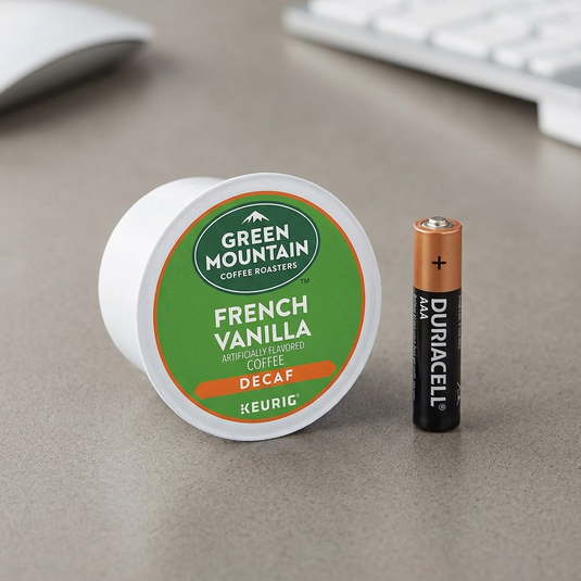 A Green Mountain French Vanilla Decaf K-Cup sitting next to a generic AAA battery.