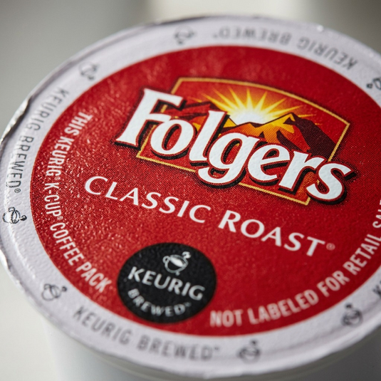 Macro detail shot of the Folgers Classic Roast K-Cup foil lid, highlighting the texture and clear printing.