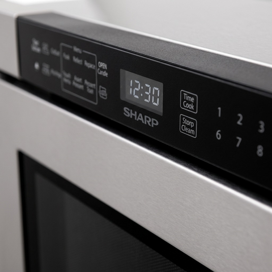 An extreme close-up photograph of the electronic control panel on the SHARP SMD2443JSC Built-In Microwave Drawer. The image shows detailed touch controls, a clear digital clock display showing "12:30", and the prominent "SHARP" logo, all illuminated under premium, low-angle lighting on the matte black interface surface. The depth of field is shallow, highlighting the precise details and reduced purchase hesitation.